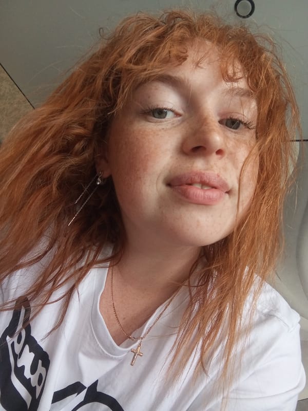 Young woman with red hair photographed wearing cross necklace