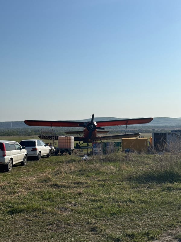 Biplane parked beside white cars in Ussurijsk field