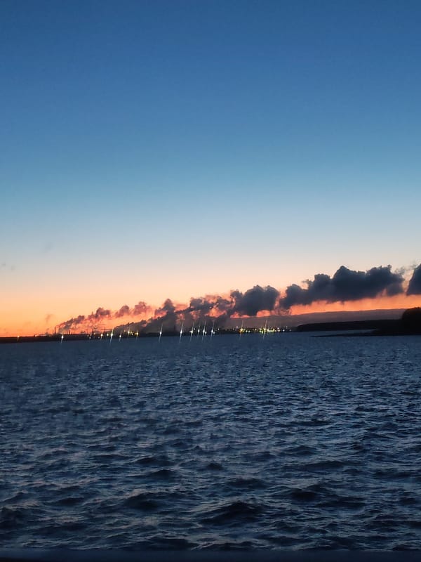 Industrial waterfront scene documented at dusk with illuminated vessels