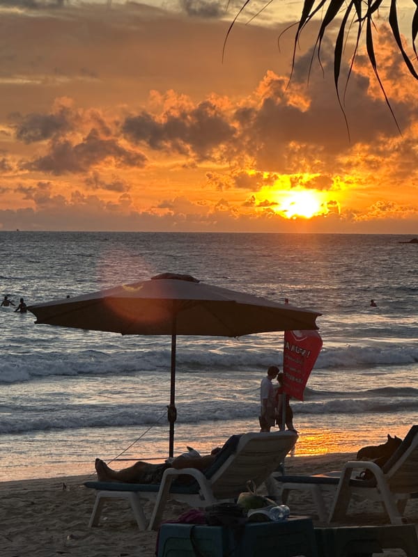 Karon Beach sunset with parasailing, boats, and beachgoers