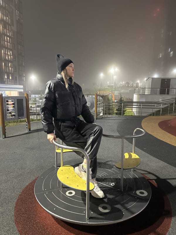 Person in black sits on playground merry-go-round at night