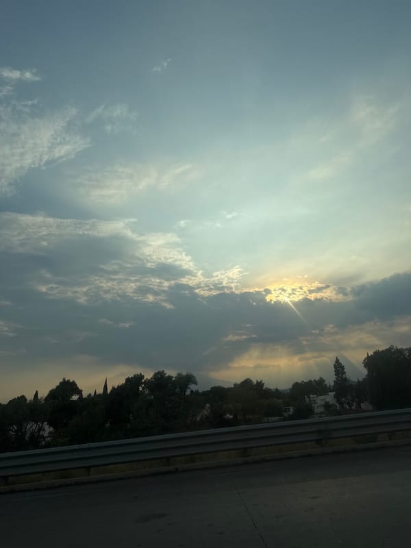 Cloudy skies with breaking sunlight observed over roadside area