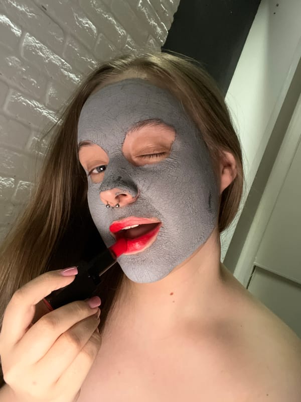 Person applies red lipstick to grey face mask