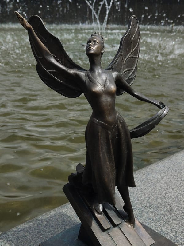 Bronze winged statue observed near fountain at coordinate location