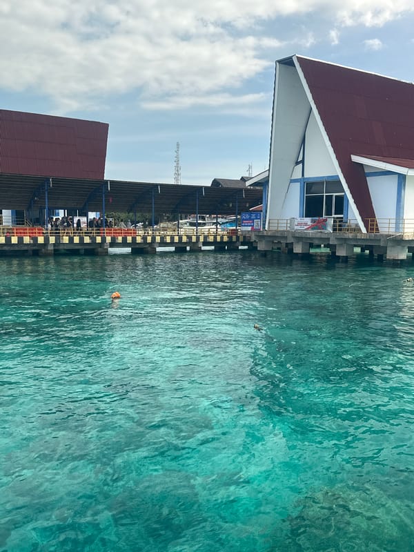 Boats navigate Indonesian waters near pier with mountainous backdrop