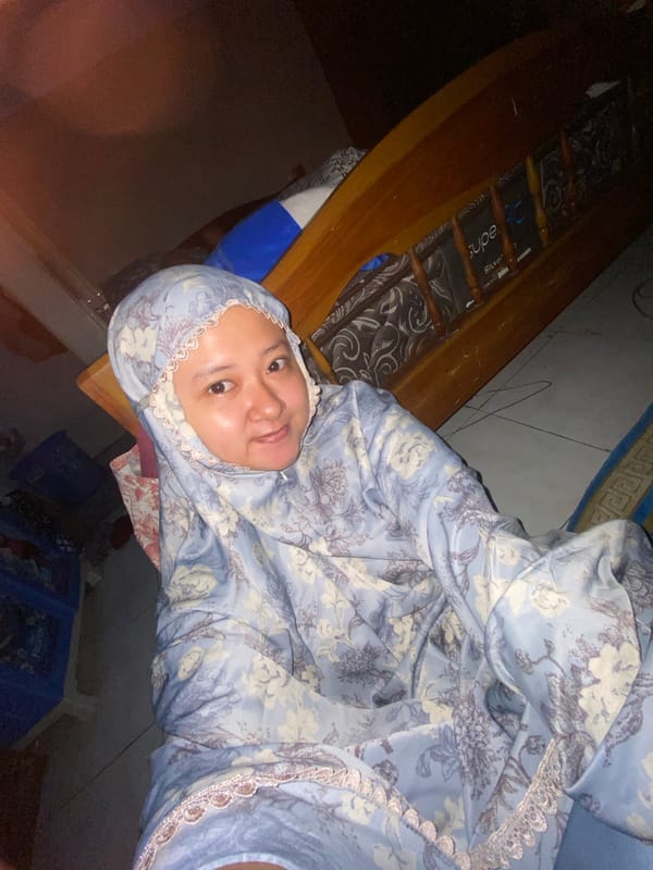 Woman in floral hijab rests on bed in Gelam
