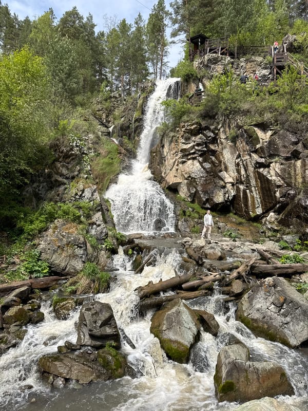 Person stands at waterfall amid lush vegetation in Barangol