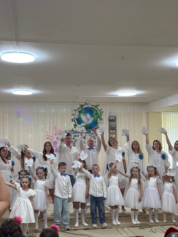 Children in white dresses gather indoors with adults