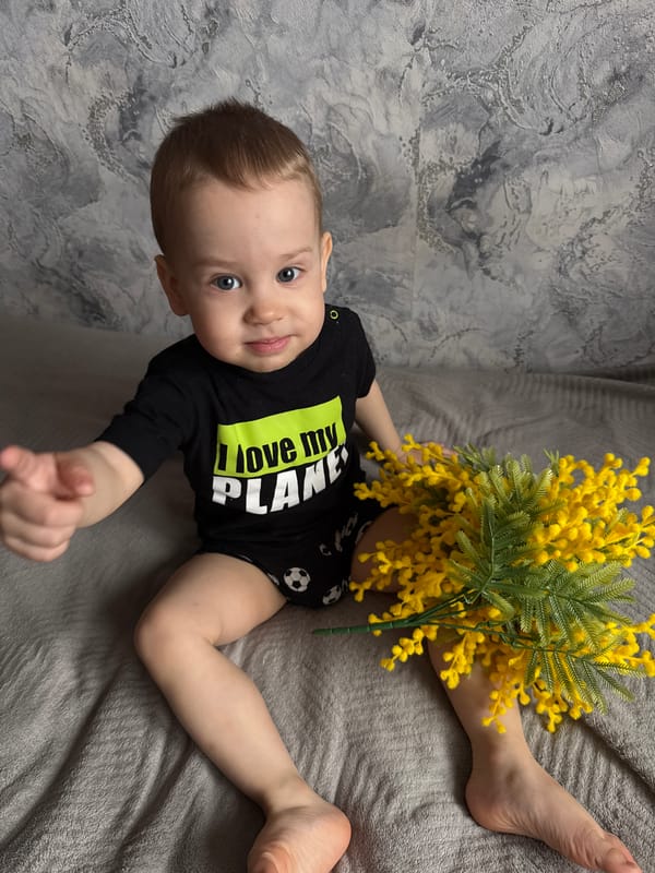 Baby photographed in eco-themed outfit with flower arrangement