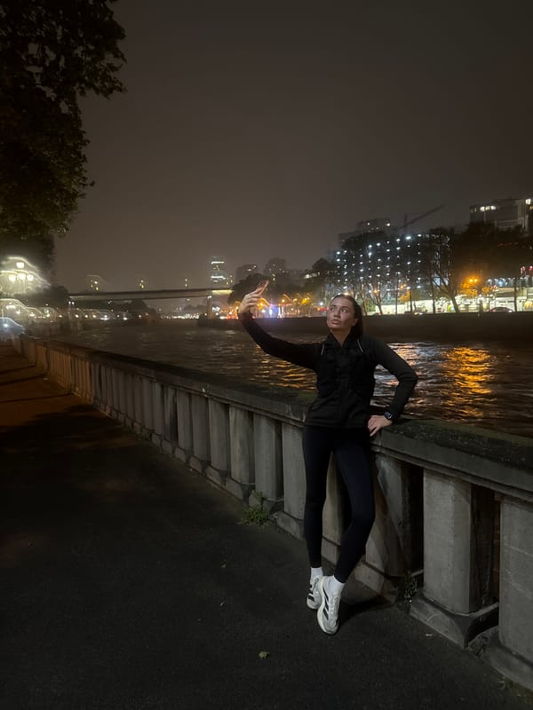 Woman poses with phone on riverside wall in Tbilisi
