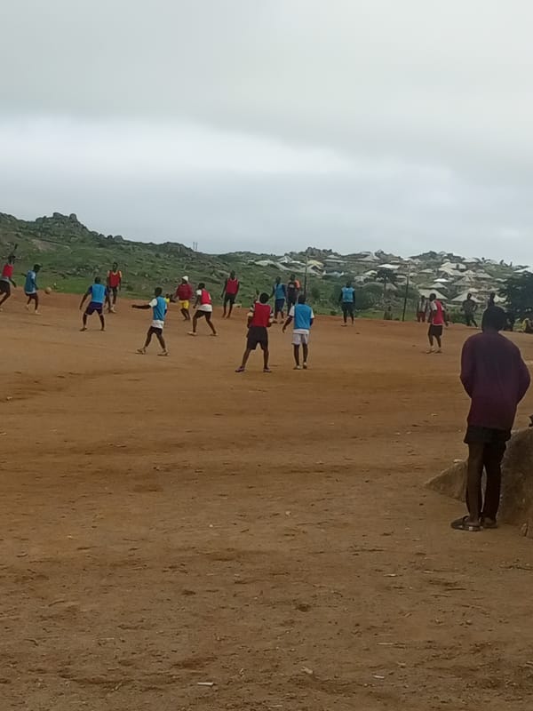 Morning soccer on a Jos dirt field amid rocky plateau terrain