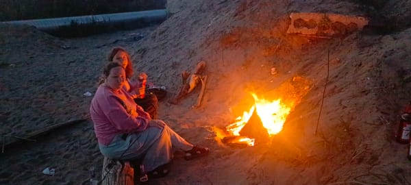 Sitting by a campfire on sandy ground at dusk