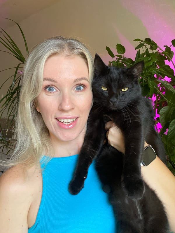 Holding a black cat on camera, mic clipped, blue tank top.