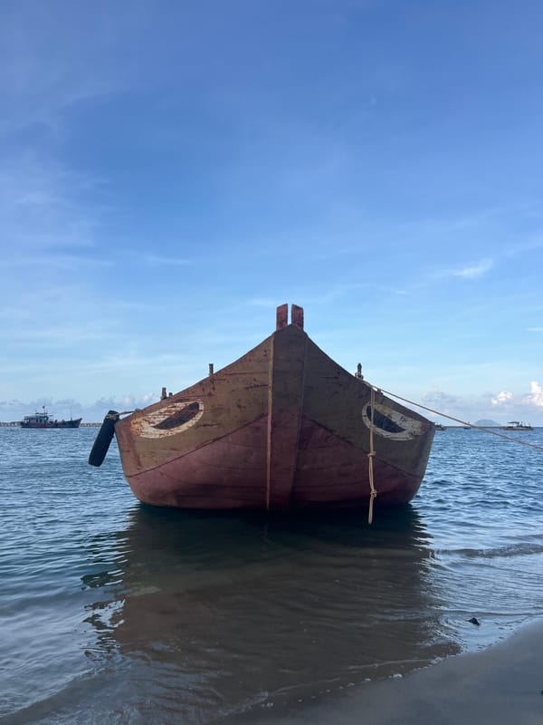 Worn red fishing boat moored in Hoi An's shallow coastal waters