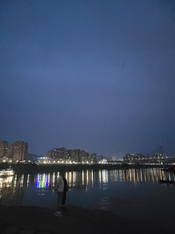Individual stands by water viewing city lights in Shapingba