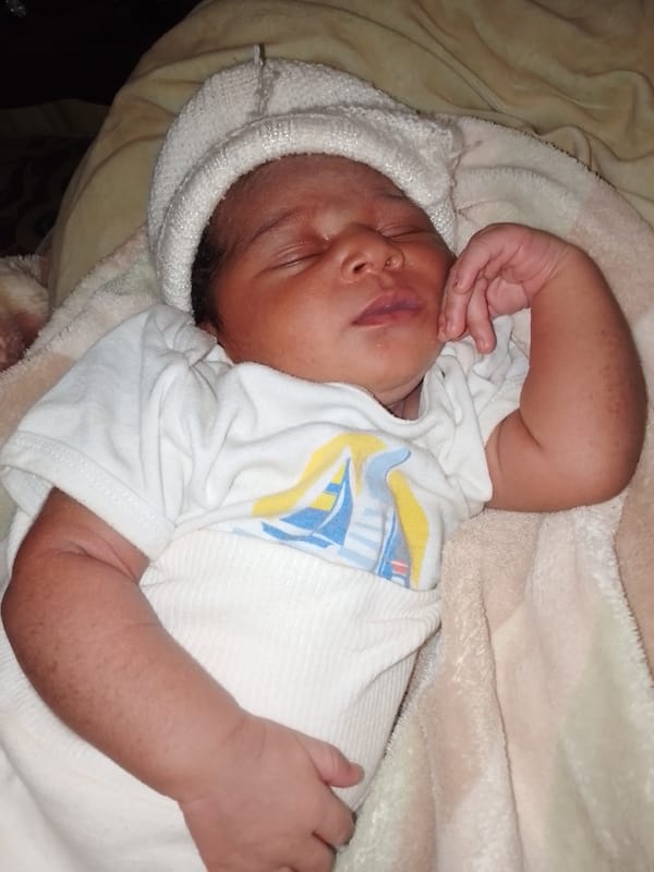 Newborn photographed sleeping in white knit hat and sailboat onesie