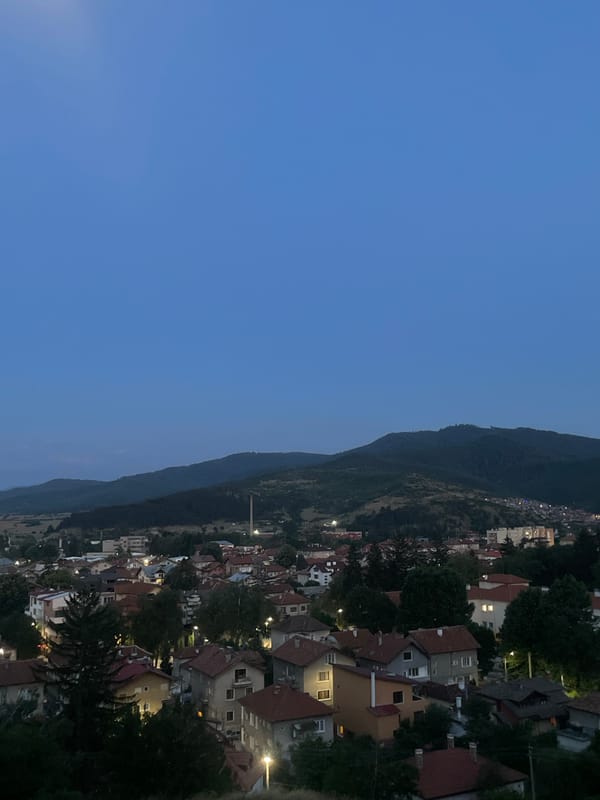 Hilltop town at twilight, forested slopes glowing with evening lights