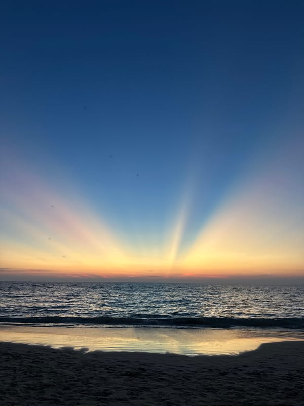 Woman photographs dramatic sunset with crepuscular rays at Thai beach