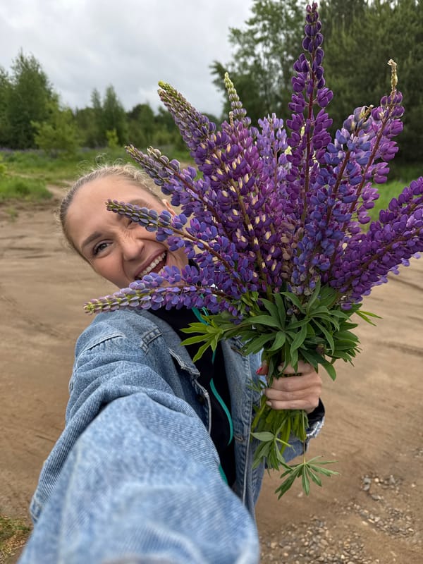 Woman poses with lupine bouquet on rural road in Chaikovsky
