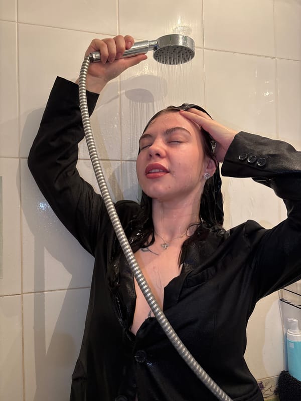 Woman in blazer lies on bathroom floor under shower