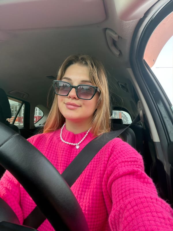 Woman in pink sweater poses playfully in car in Agryz