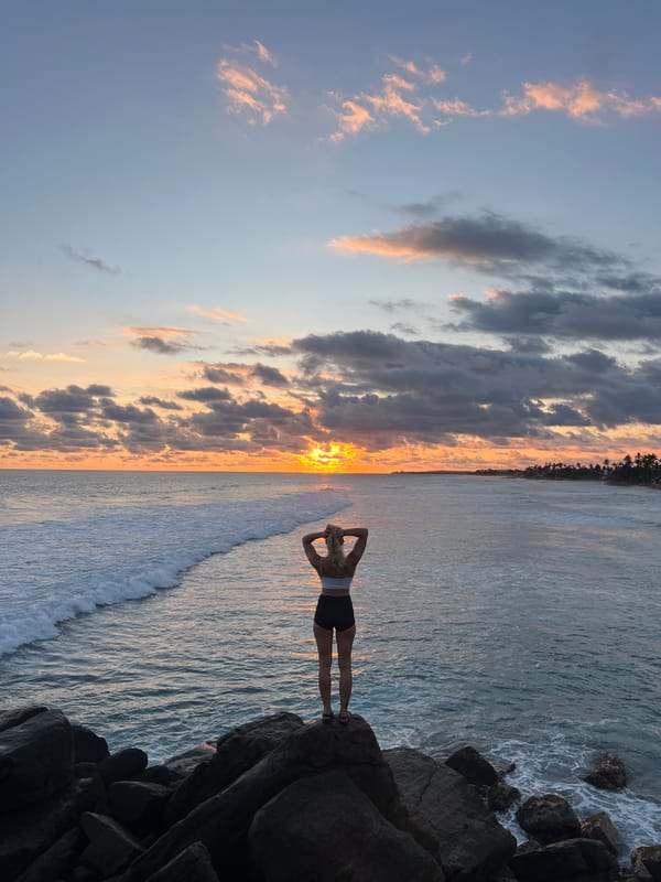Woman poses on rocks during dramatic sunset at Goviyapana beach