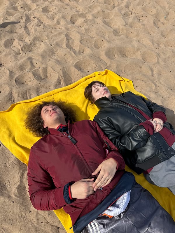 Two people rest on yellow towel at beach