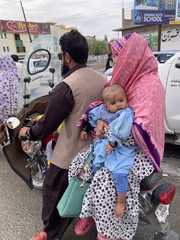 Family travels by motorcycle through Quetta streets under overcast sky