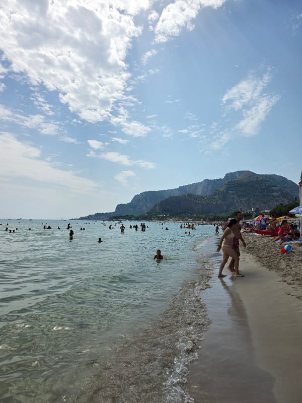 Crowded beach day with calm water and a mountain backdrop