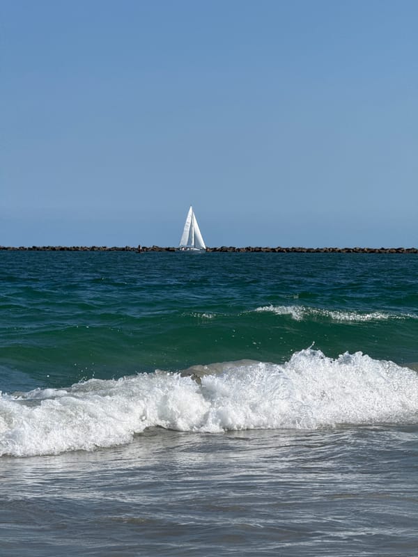 Sailboat cruising past Wrightsville Beach breakwater on calm day
