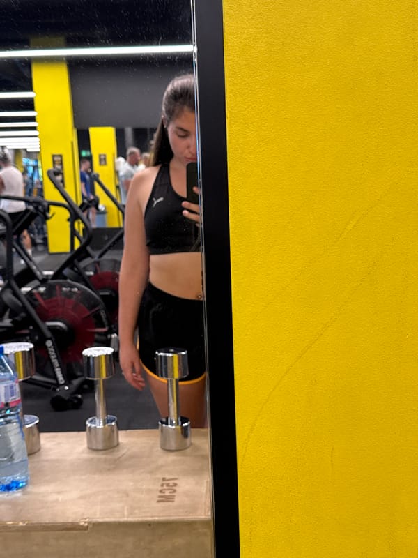 Gym selfie captured in mirror showing yellow wall detail