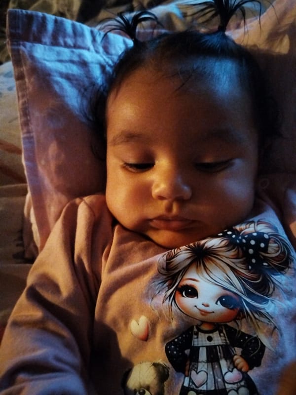 Baby with ponytails rests on pink pillow wearing cartoon shirt