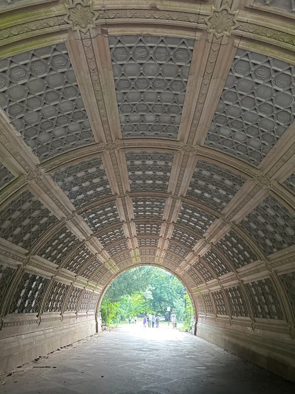 Looking through a decorative stone tunnel into a sunlit park path