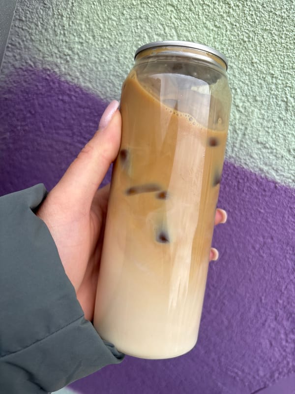 Person holds layered iced coffee against colorful wall in Sofia