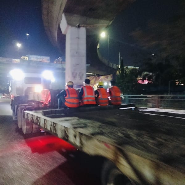 Construction workers rest on truck trailer under Dhaka bridge