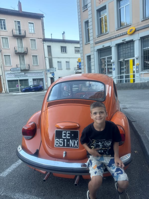 Afternoon street scene in Saint-Claude with an orange Beetle and a balance bike.