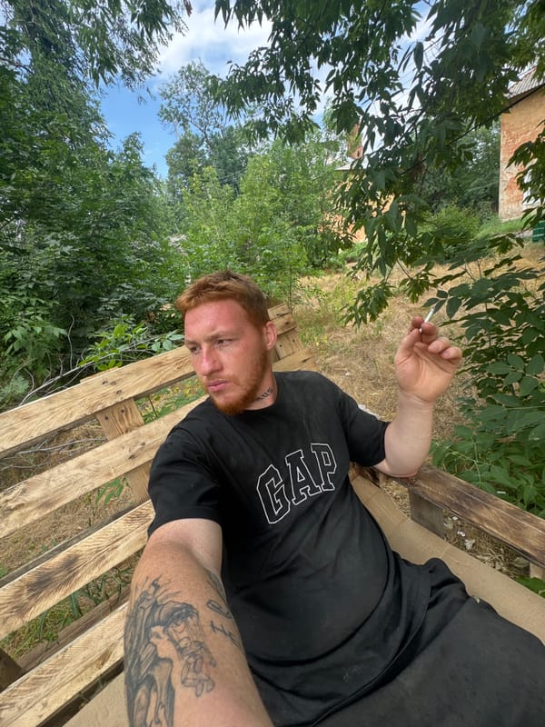 Sitting on a pallet bench outdoors, GAP tee, mid-smoke