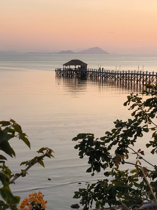 Labuan Bajo waterfront at golden hour — piers, cannons, and bougainvillea
