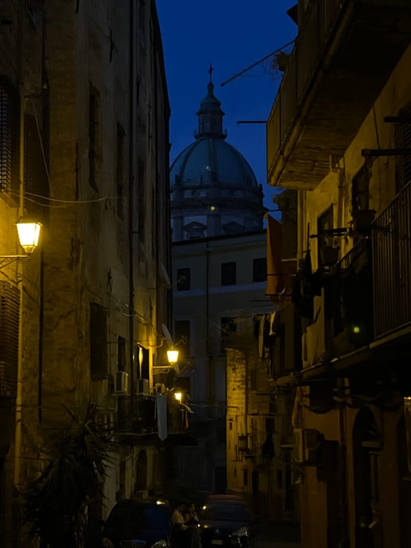 Domed church silhouette over a narrow Palermo street at dusk