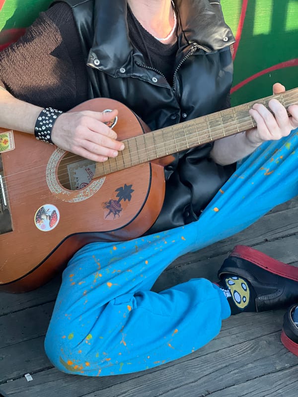 Street musician plays guitar on Belgrade deck wearing paint-splattered pants