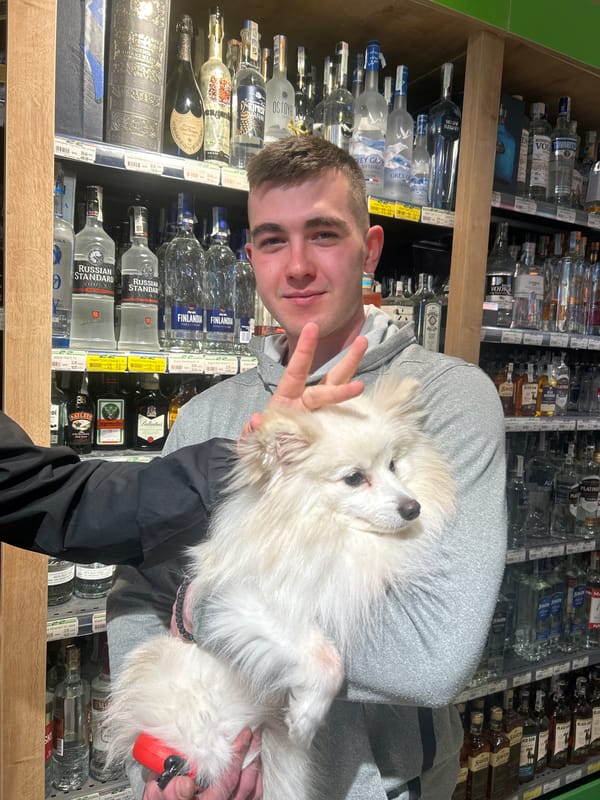 Man holds fluffy white dog in Bulgarian store alcohol aisle