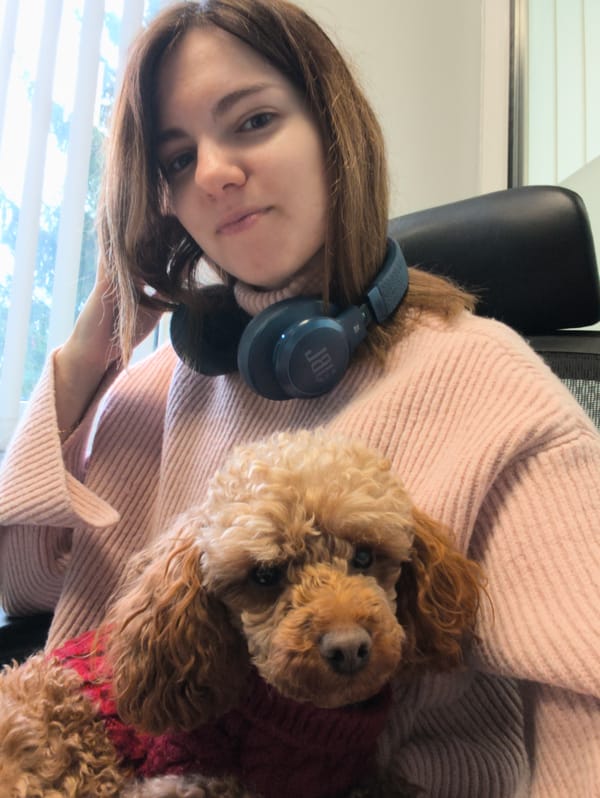 Woman with headphones holds poodle in red sweater