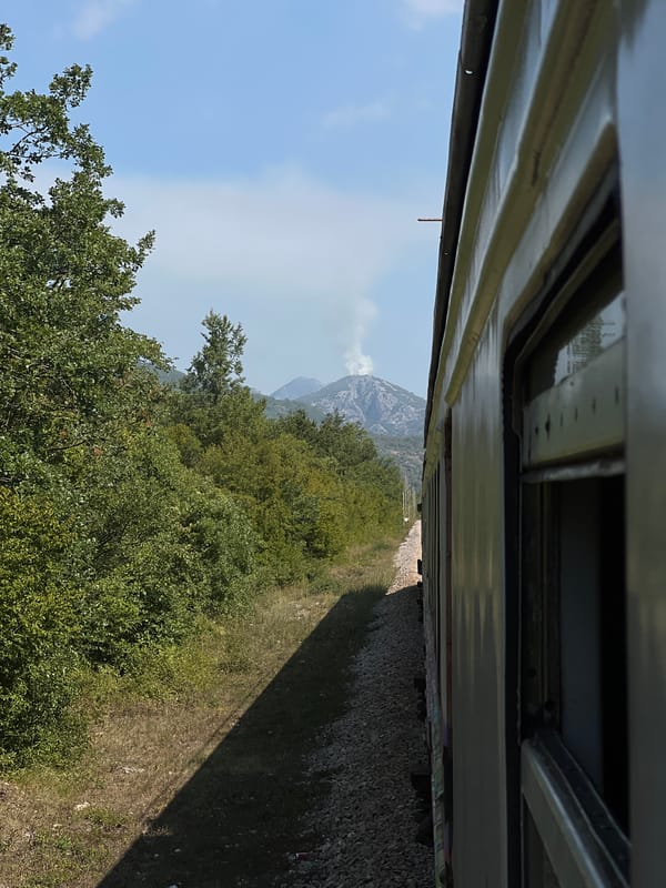 Smoke rising from a mountain peak, seen from a passing train