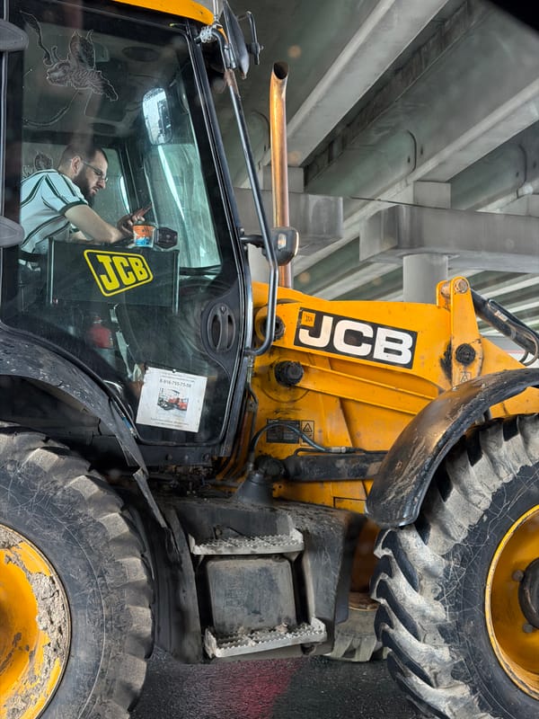 Construction worker operates backhoe while holding unidentified object