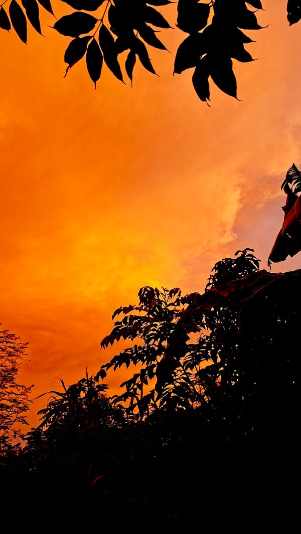 Fiery sunset sky over Kutaglumpang, framed through trees and doorways.