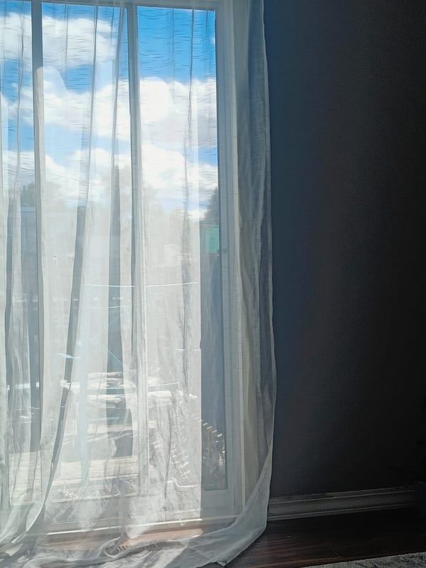 Evening sunlight illuminates sheer curtains in dimly lit room