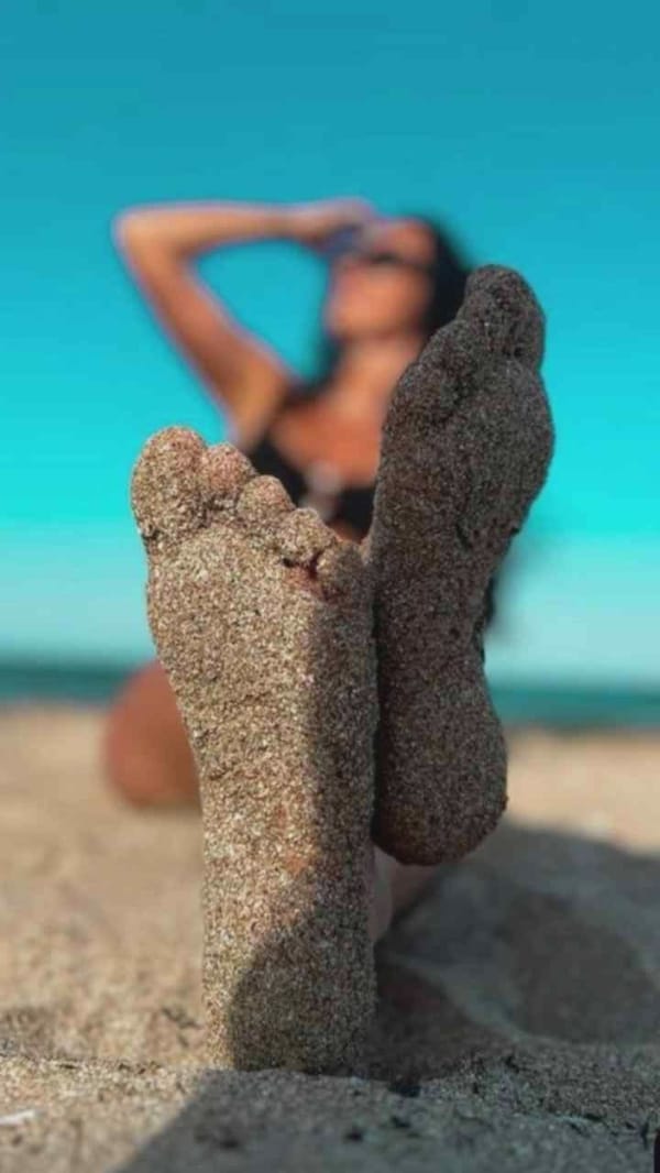 Beach scene captured showing sandy feet with bikini-clad figure