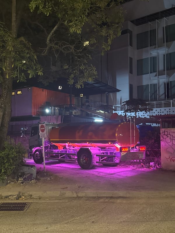 Neon-lit tanker truck parked on a Ko Samui dirt road at night
