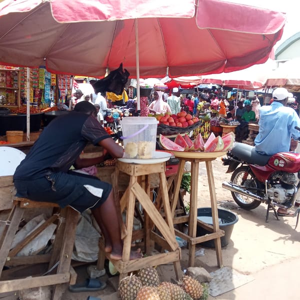 Vendors operate under red umbrellas in Akwanga marketplace