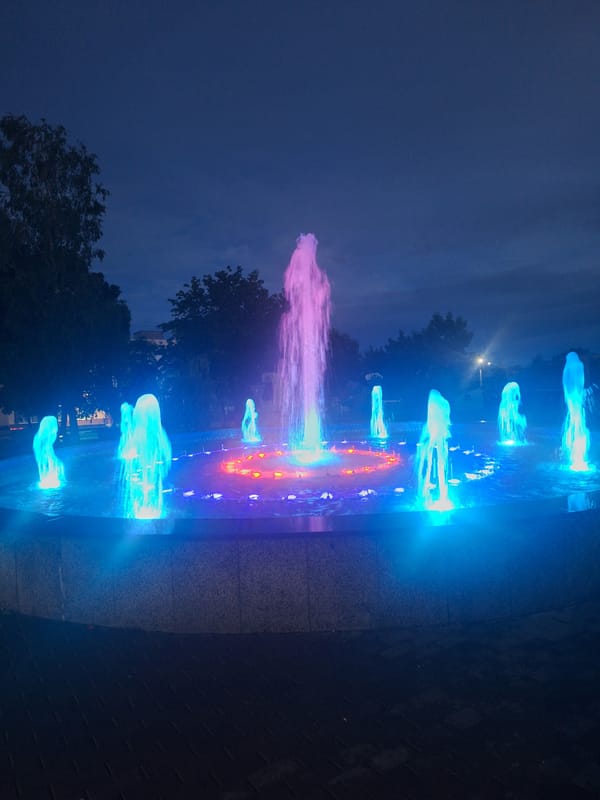 Kapyĺ's lit fountain and rainy evening streets at dusk